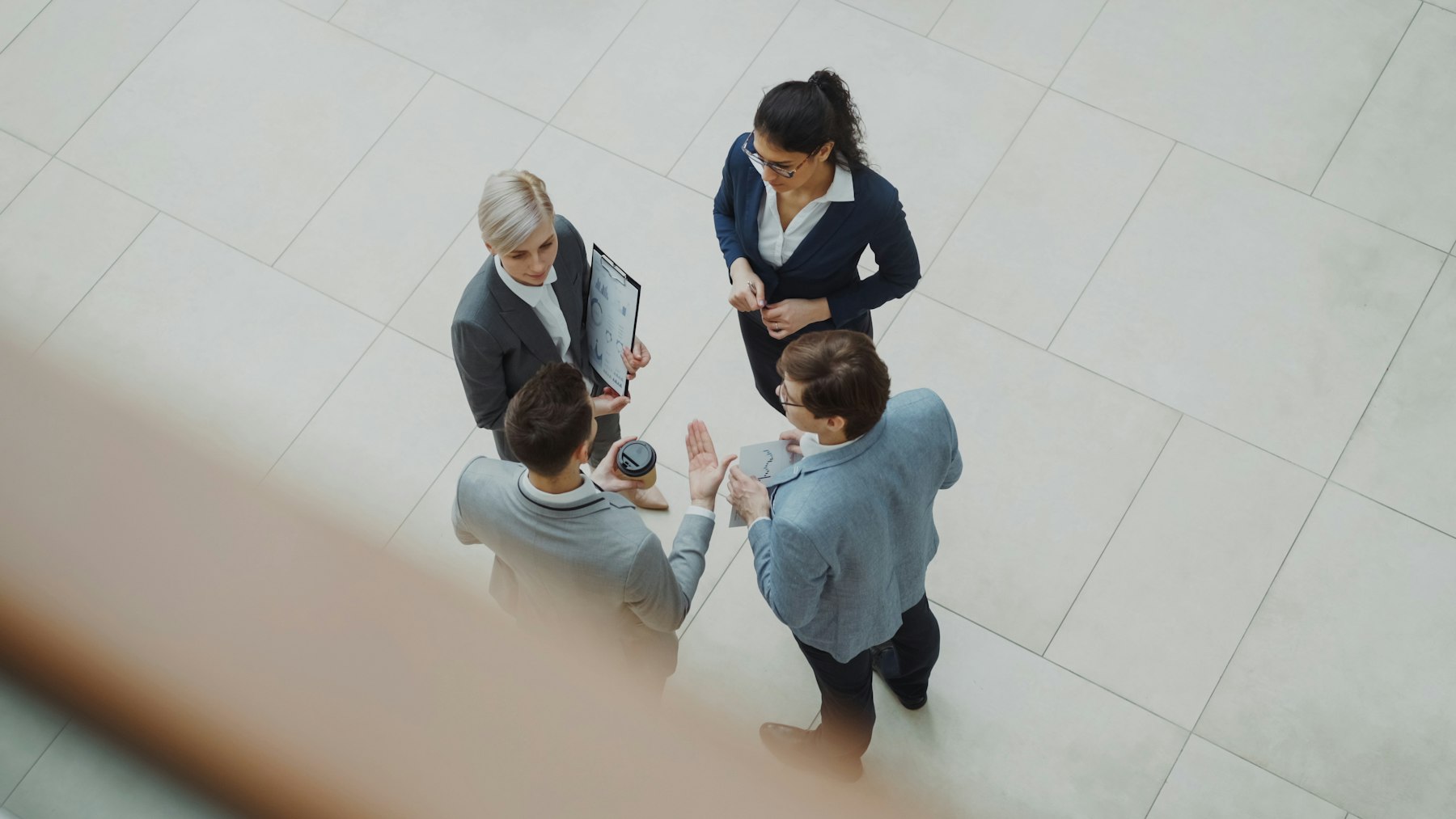 Four business professionals talk together in a modern office lobby